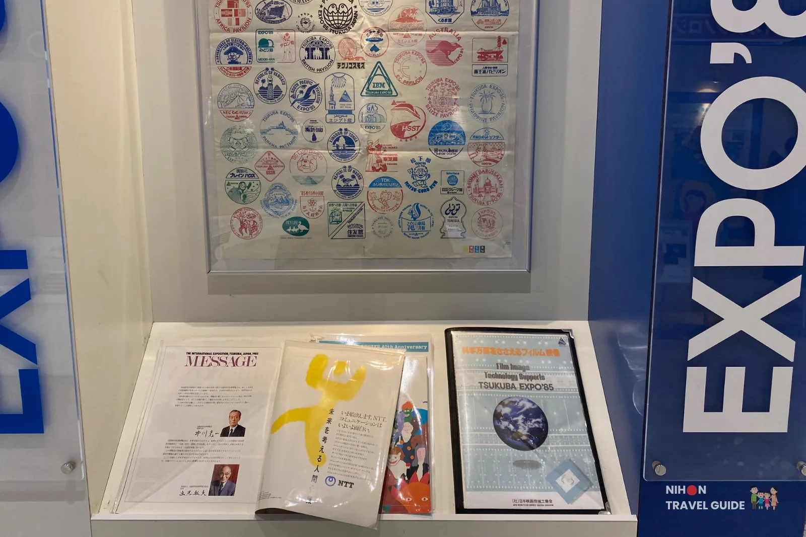 Display of colorful commemorative stamps and seals from international and Japanese pavilions at the 1985 Tsukuba Expo, shown alongside other memorabilia.