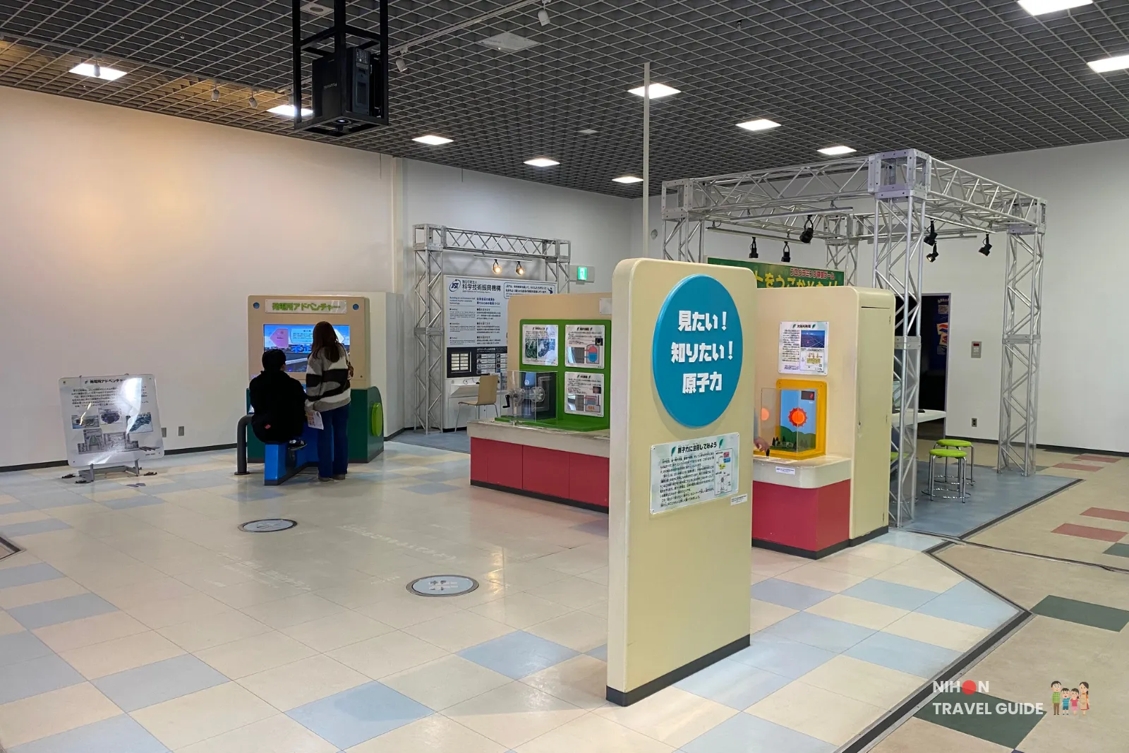 Interactive exhibits in the Fun Science Zone, including the “Atom Force” (原子力) station and other hands-on science displays with colorful flooring and metal truss structures.