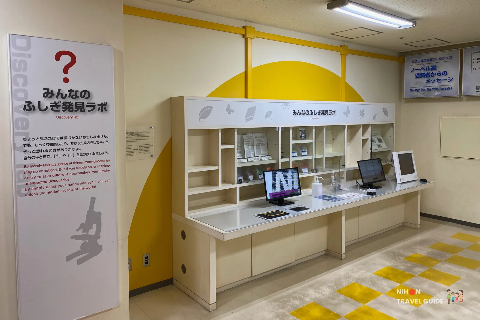 Discovery Lab (みんなのふしぎ発見ラボ) in the Fun Science Zone at Tsukuba Expo Center. This hands-on corner includes display shelves, monitors, and encouraging signage to spark curiosity and observation skills.