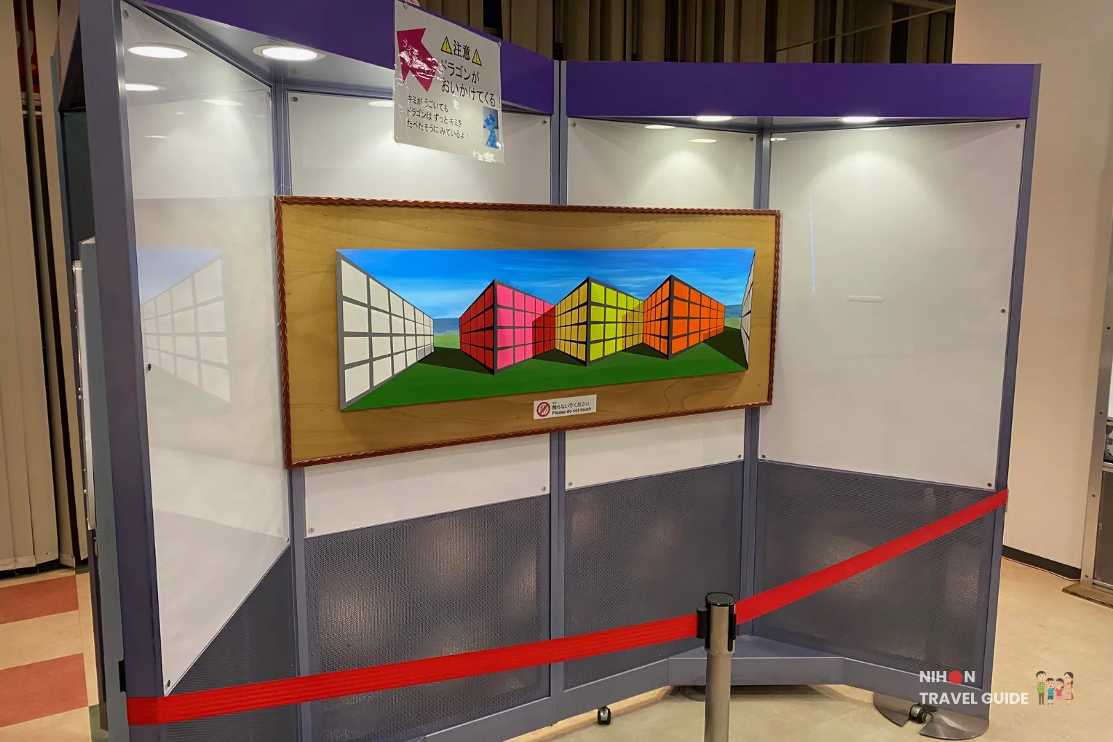 Optical illusion exhibit in the Fun Science Zone at Tsukuba Expo Center. The colorful dragon artwork appears to follow visitors as they move, with a warning sign not to touch the display.