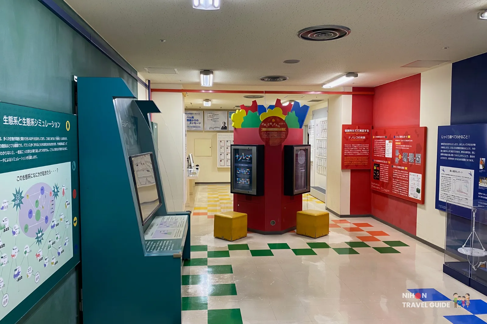 Interactive exhibition area in the Fun Science Zone on the first floor of Tsukuba Expo Center. Features colorful hands-on stations, simulation panels, and life science exhibits with a checkered floor pattern.