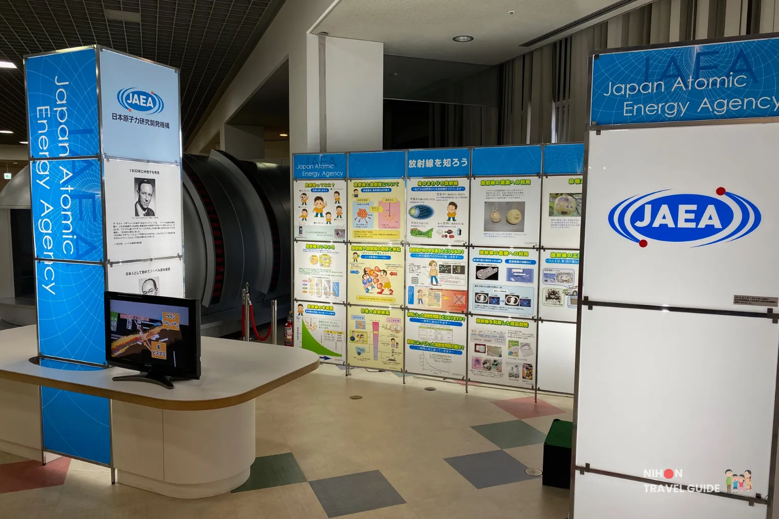 Japan Atomic Energy Agency (JAEA) exhibition corner in the Fun Science Zone at Tsukuba Expo Center. Large blue panels explain radiation, nuclear energy, and peaceful uses of atomic technology with colorful illustrations and displays.