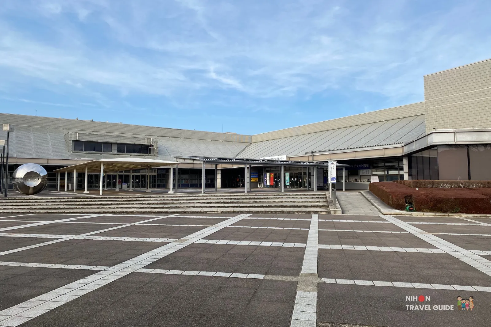 Wide view of the main entrance and plaza at Tsukuba Expo Center, showing the broad steps, covered walkway, and modern architecture of the science museum.