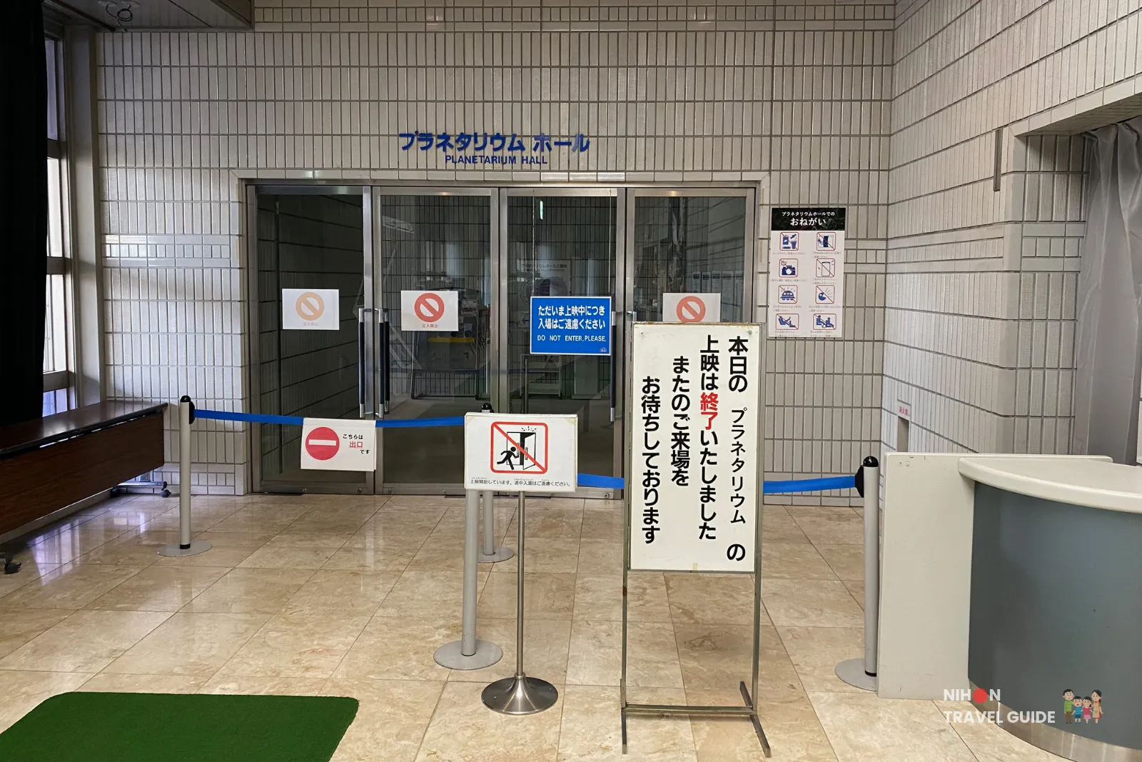 Entrance to the Planetarium Hall at Tsukuba Expo Center. The doors are currently closed with signs indicating "Do Not Enter" and that today's shows have ended. Blue retractable barriers guide visitors.