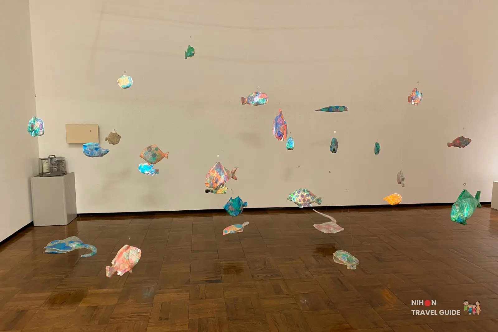 Colorful hanging fish sculpture installation at University of Tsukuba Master’s Degree Exhibition — multicolored patterned fish suspended from the ceiling and resting on the wooden floor.
