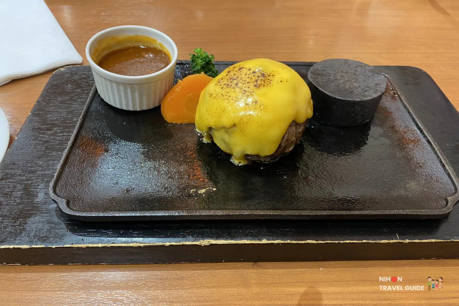 Hamburg steak topped with rich yellow cheese sauce served on a hot plate at Smile Hambarg, Fashion Cruise Newport.