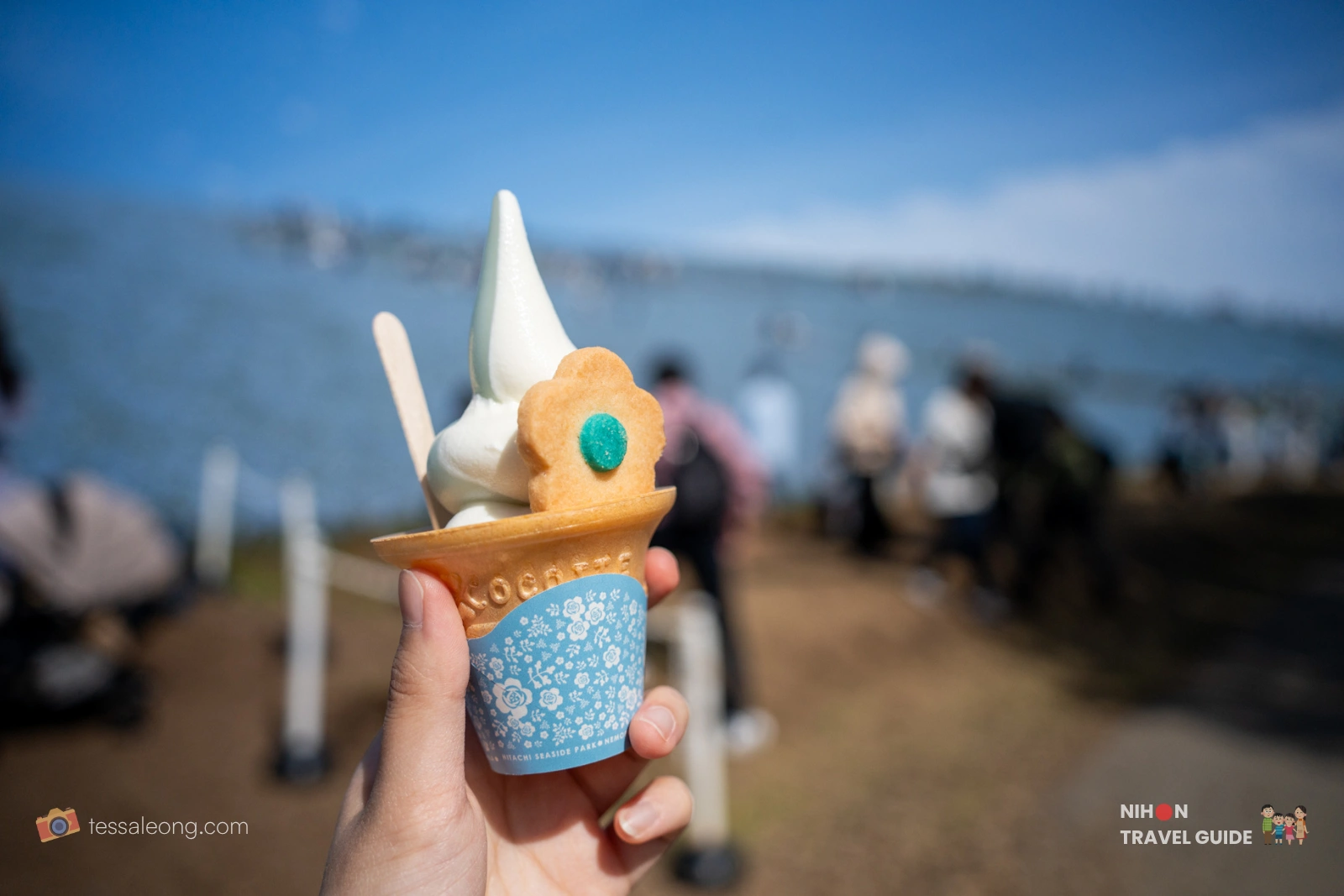 Nemophila Soft Serve ice cream held in hand at Hitachi Seaside Park, with the ocean and flower fields in the background.