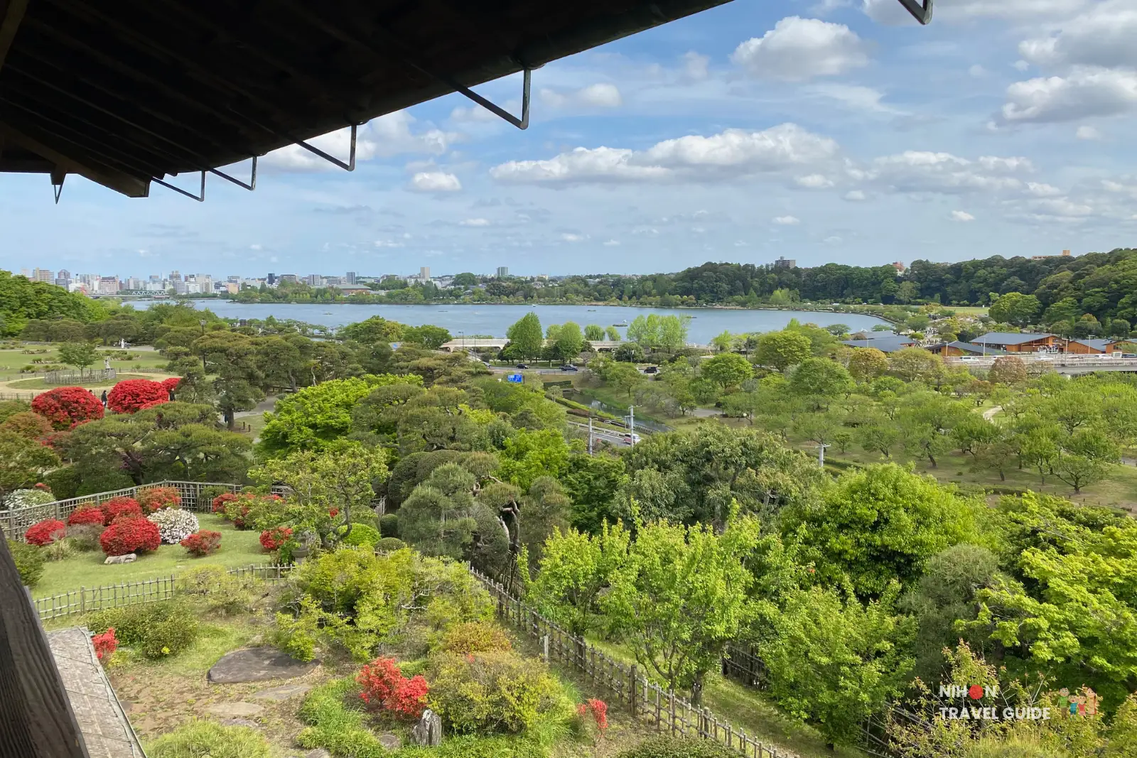 lake-senba-view-kobuntei Panoramic view of Lake Senba from Kobuntei, showing the expansive lake, lush gardens with red azaleas, and the Mito city skyline in the distance.