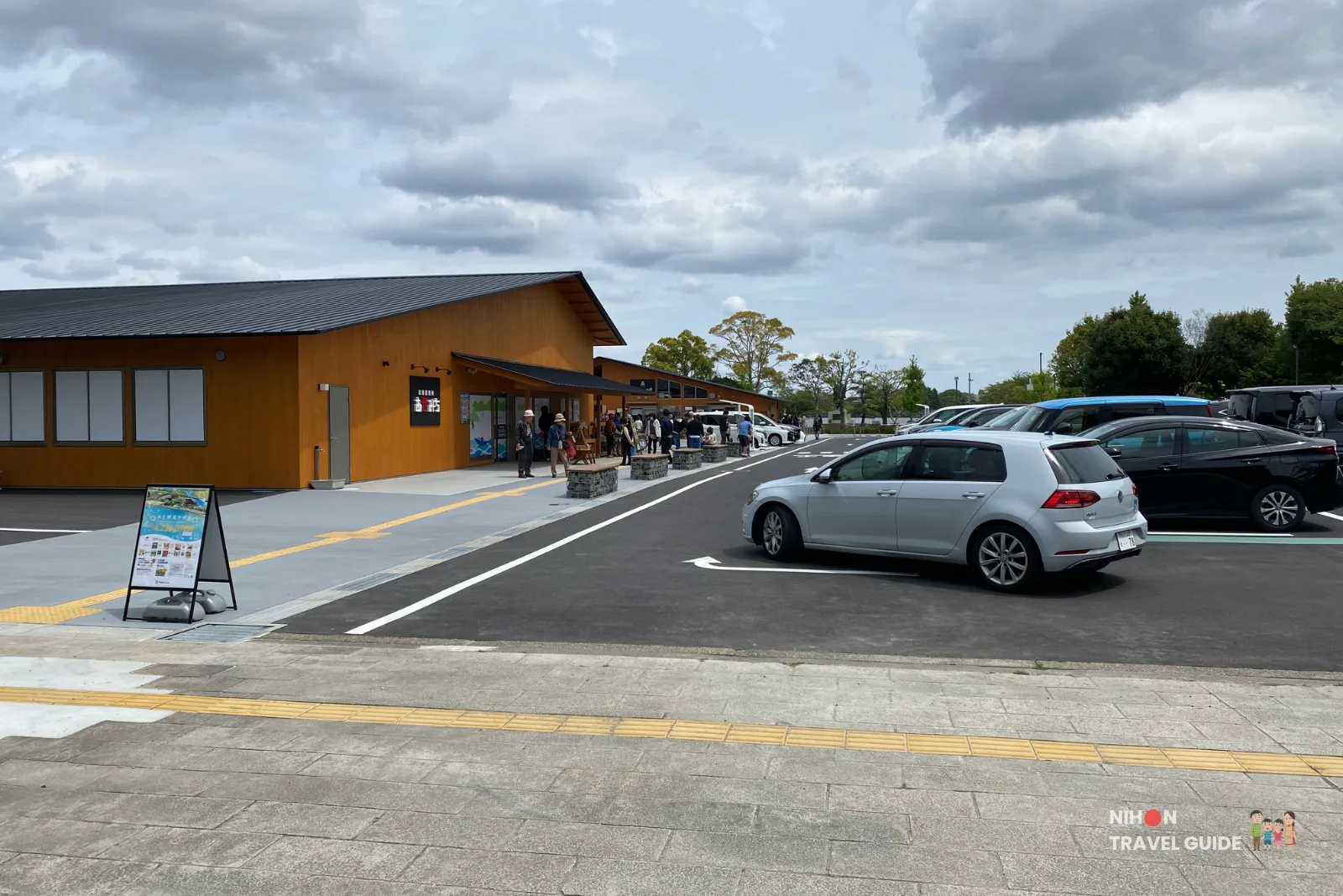 Overview of Mito Kobun Terrace buildings and parking area, showing the new wooden architecture and visitors on a cloudy day near Lake Senba.