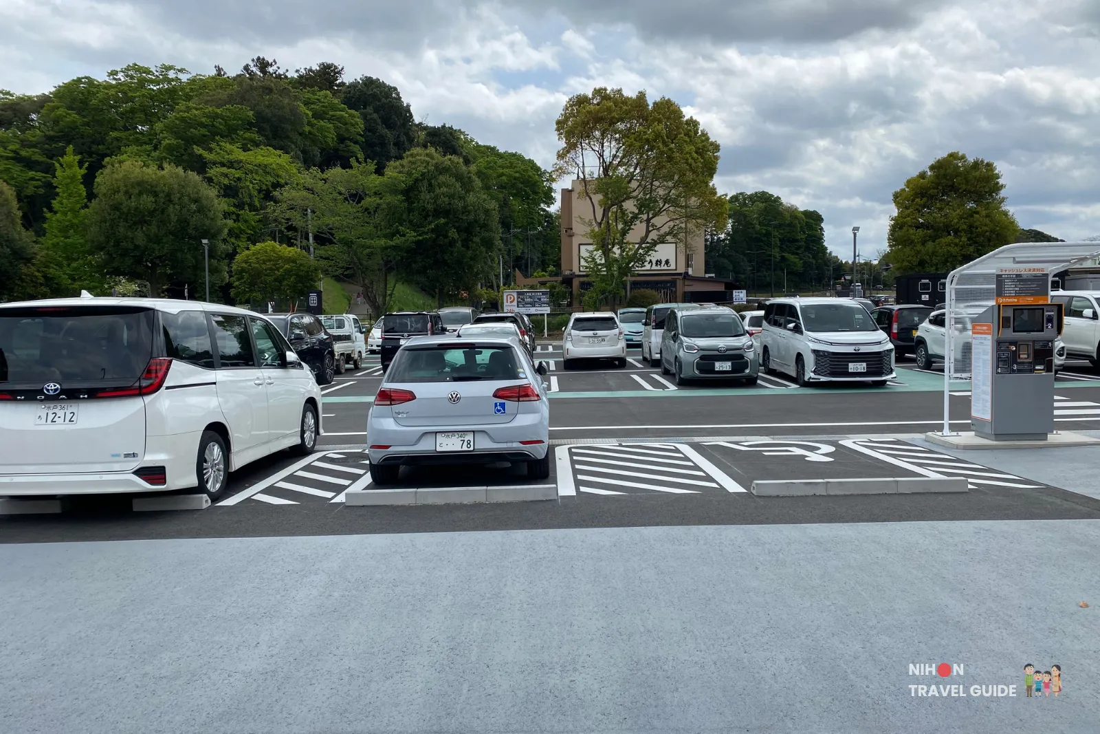 mito-kobun-terrace-parking-lot Parking lot at Mito Kobun Terrace near Lake Senba, featuring accessible parking spaces, payment machines, and parked cars with lush greenery in the background.