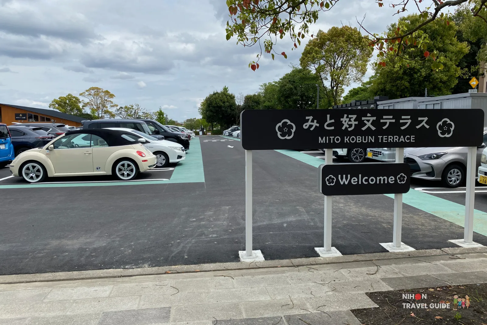 mito-kobun-terrace-welcome-sign-parking Welcome sign at the parking lot of Mito Kobun Terrace (みと好文テラス), featuring the official name and logo with parked cars in the background near Lake Senba.