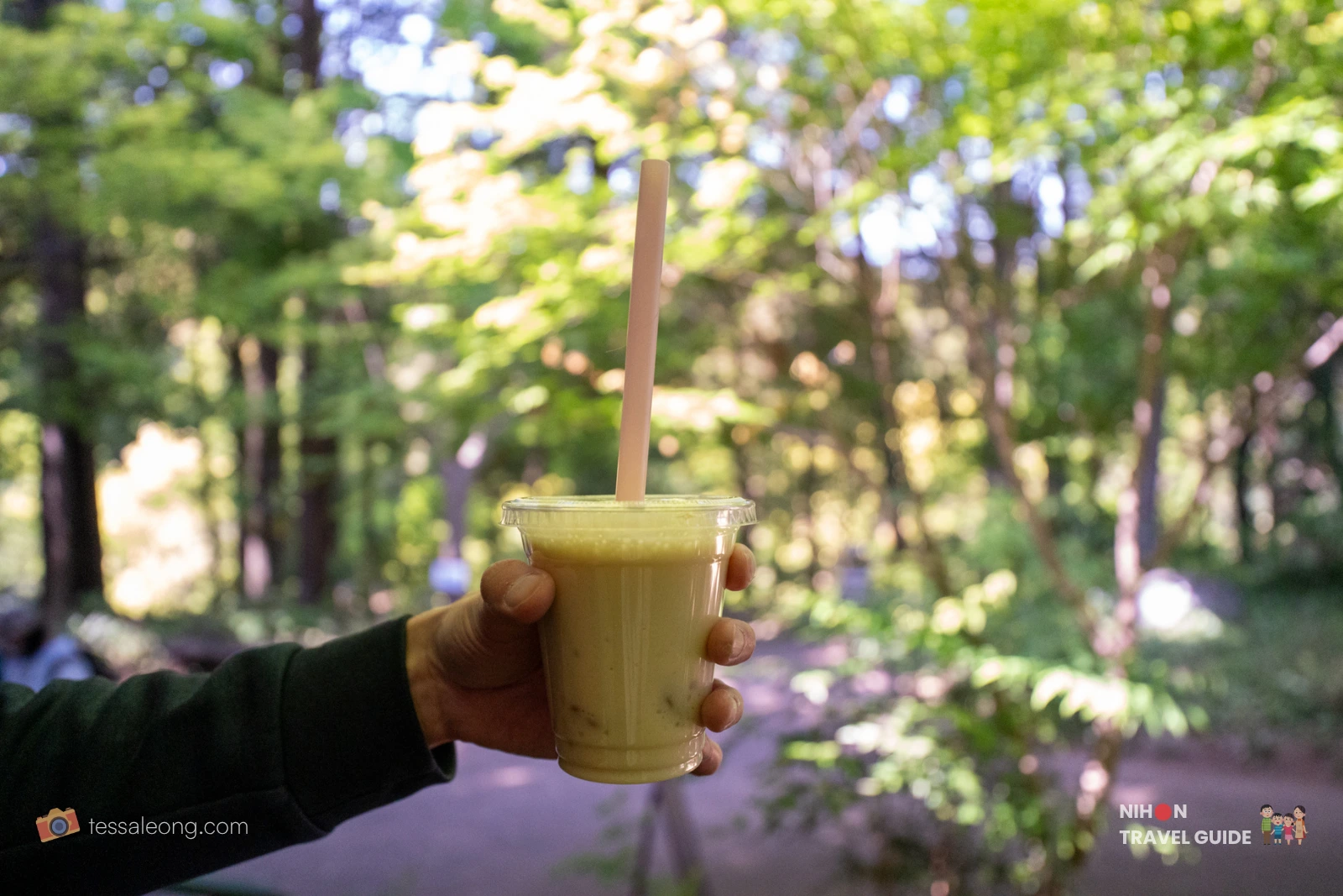 peony-garden-tokyo-harvest-cafe-sweet-potato-latte Hand holding a cup of creamy roasted sweet potato latte from Harvest Cafe at Peony Garden Tokyo, with lush green trees in the background on a sunny spring day.