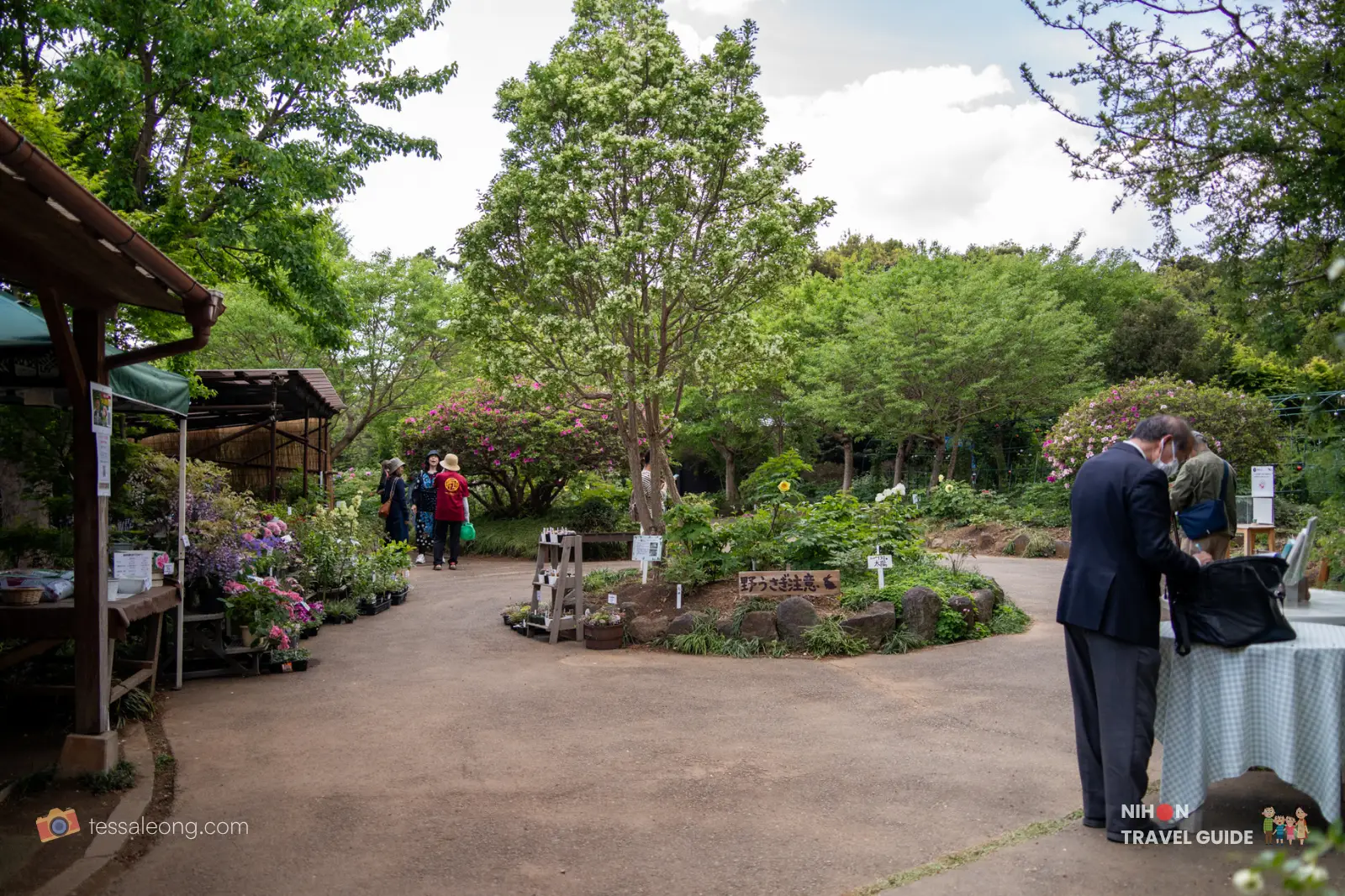 peony-garden-tokyo-main-area Main garden path and plant sales area at Peony Garden Tokyo, with potted flowers for sale on the left, visitors walking around, and lush green trees under a bright partly cloudy sky.