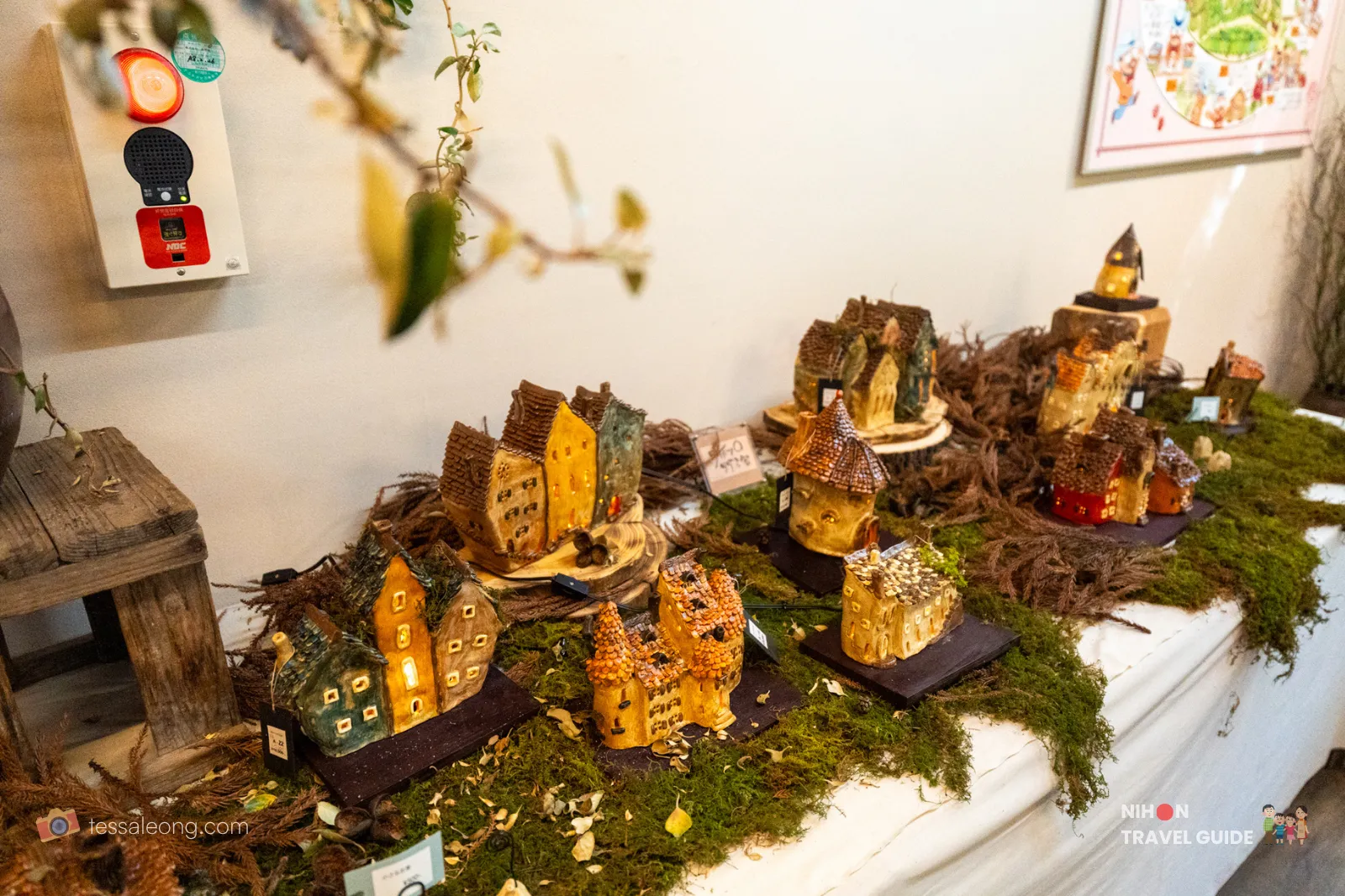 Handmade miniature ceramic fairy houses and village cottages for sale in the Harvest Cafe / Garden Shop at Peony Garden Tokyo, displayed on moss with some illuminated houses.
