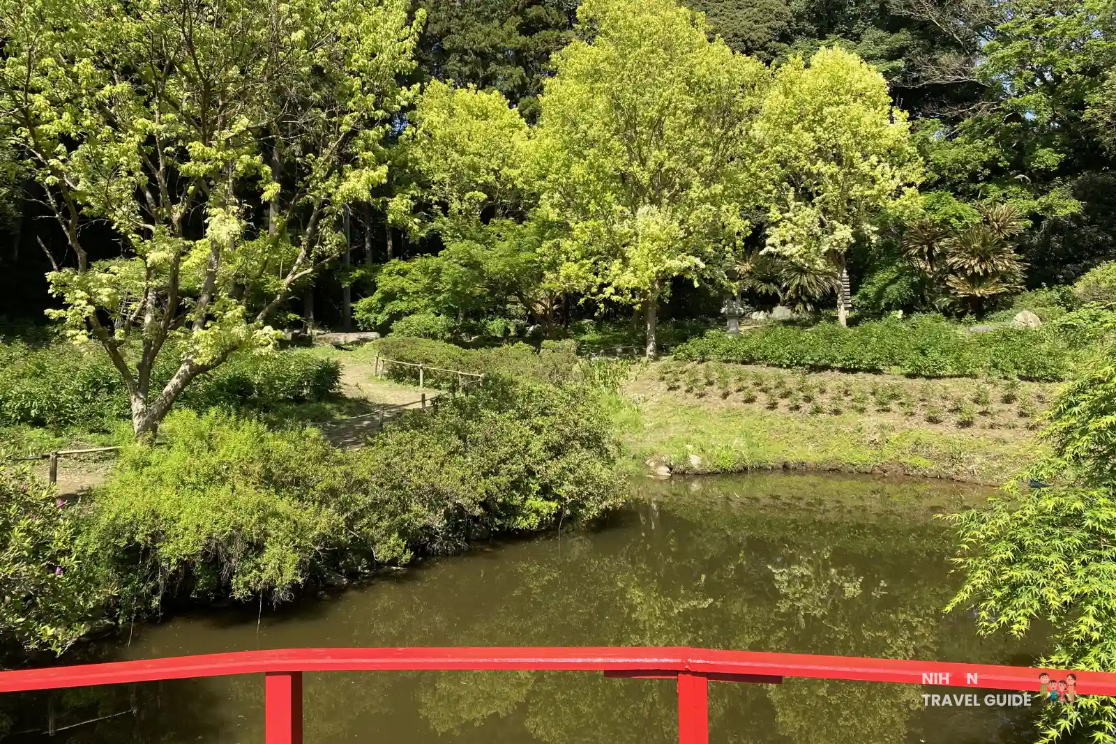 Scenic view of the pond and lush green trees at the Waterside Area (Mizube Area) of Peony Garden Tokyo, taken from the bright red bridge on a sunny spring day.