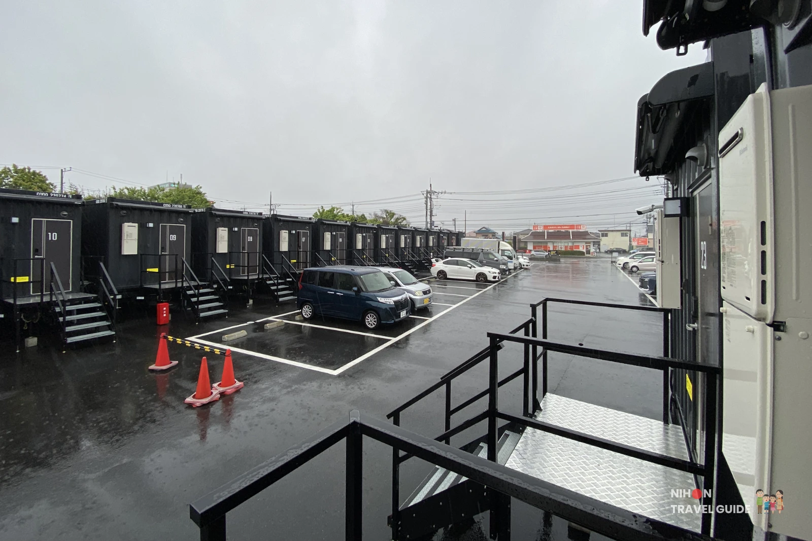 View of the black shipping container-style guest rooms and stairs at R9 The Yard Hotel Hitachinaka Ichige on a rainy day in Ibaraki, Japan