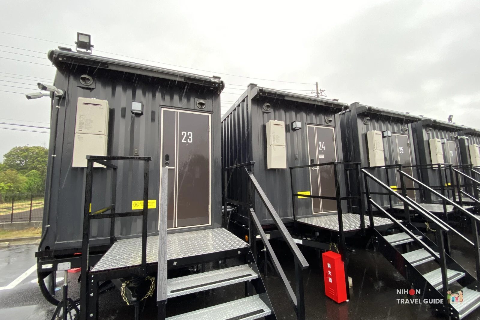 Guest rooms 23, 24, and 25 at R9 The Yard Hotel Hitachinaka Ichige – black shipping container-style units with external stairs on a rainy day