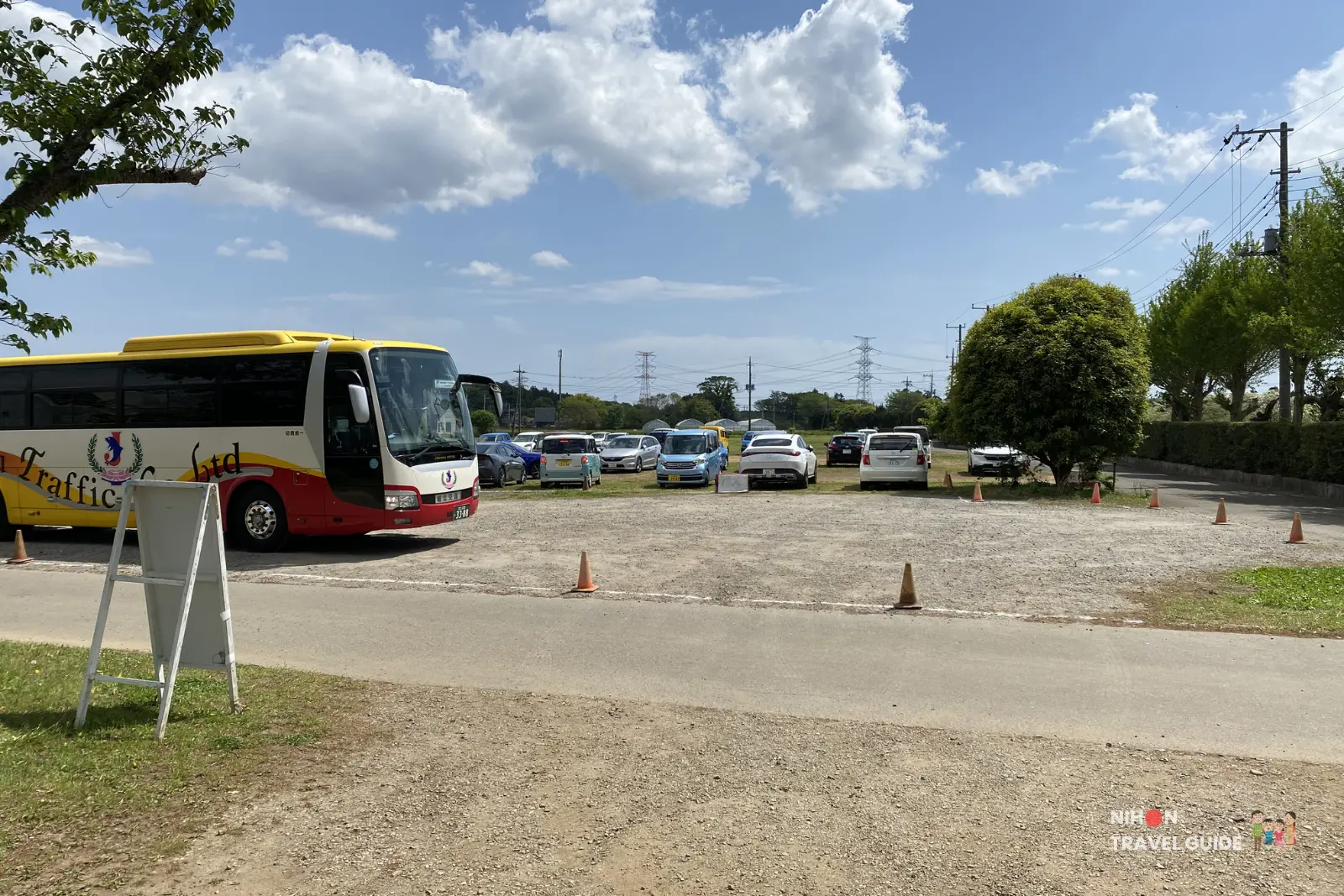 tsukuba-peony-garden-parking Spacious parking lot at Peony Garden Tokyo in Tsukuba, Ibaraki, with a yellow and red tour bus parked on the left and many private cars on a bright sunny day.