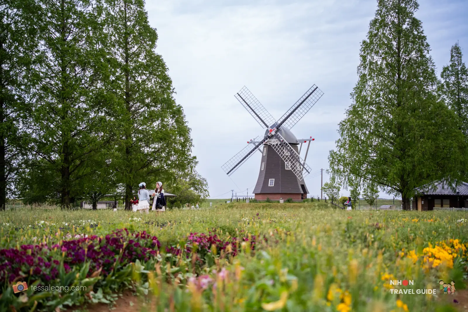Traditional windmill towering over a meadow of colorful wildflowers, with a few people strolling nearby.