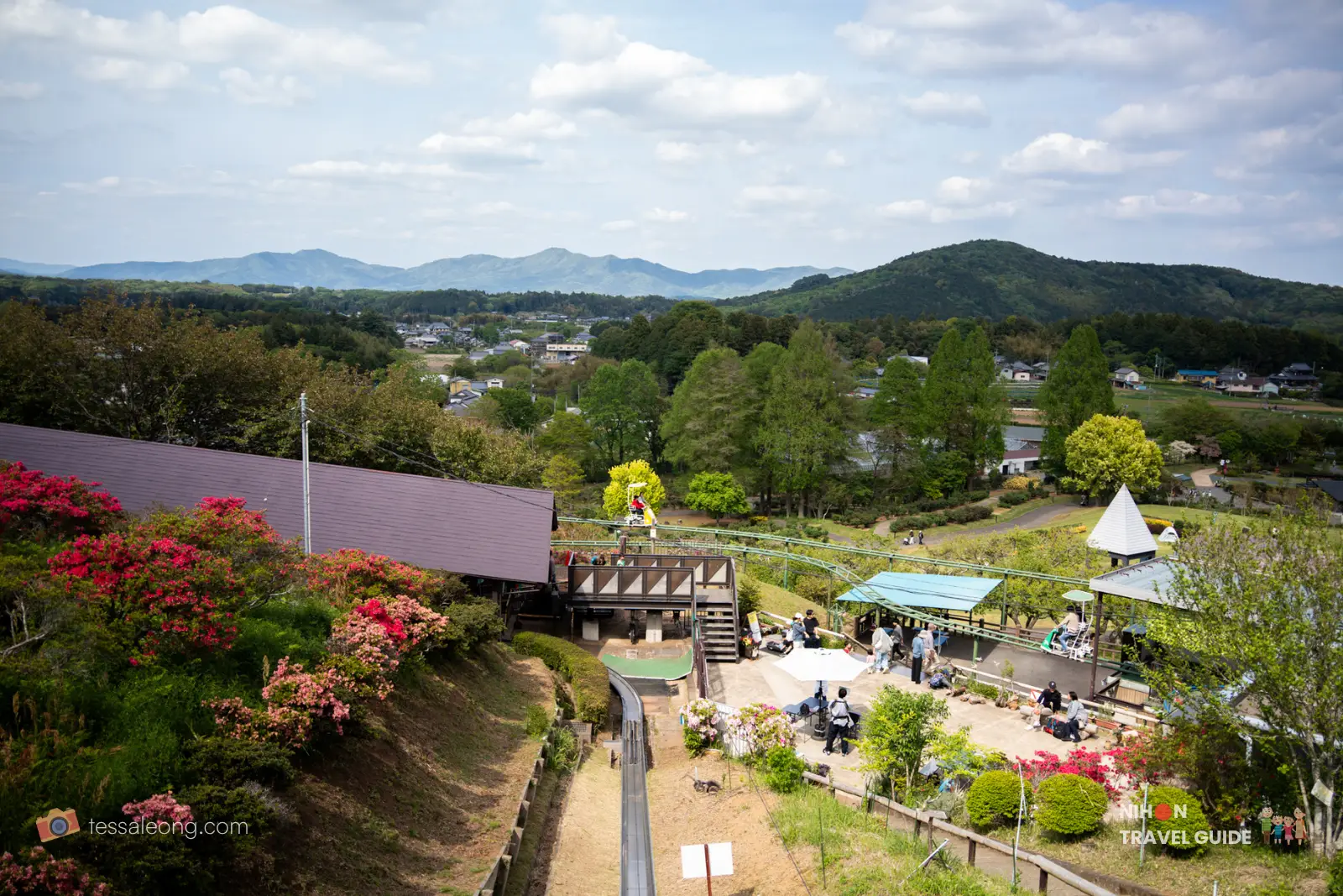 Panoramic view from Hanayasatoyama Area at Ibaraki Flower Park showing the Sky Cycle ride and surrounding gardens with mountains in the background.