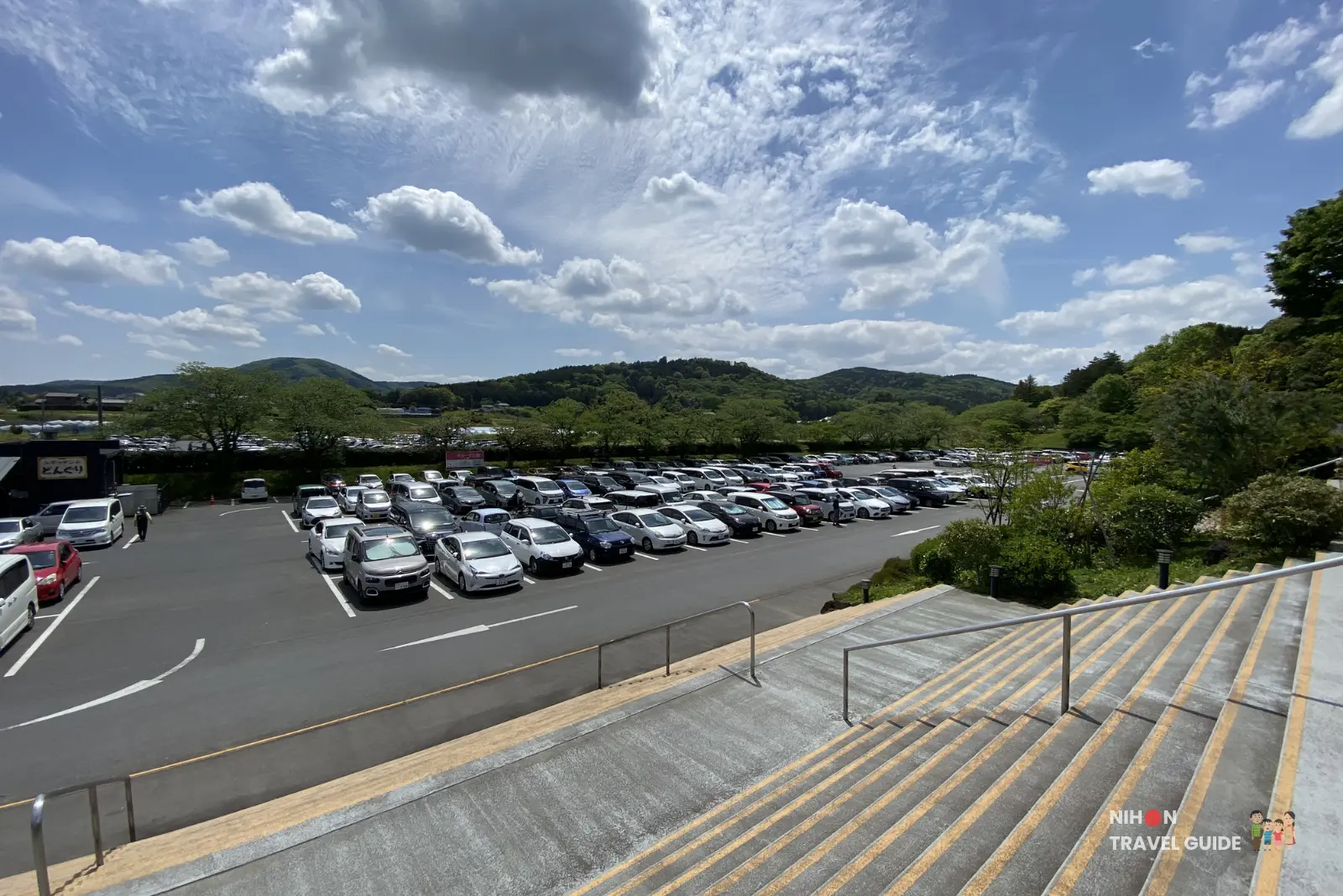 Large parking lot at Ibaraki Flower Park with many cars on a sunny day, surrounded by green hills