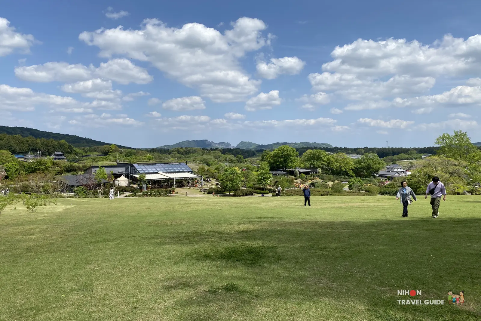 Wide scenic view of Ibaraki Flower Park with large lawn and Rose Farm House restaurant in the background.