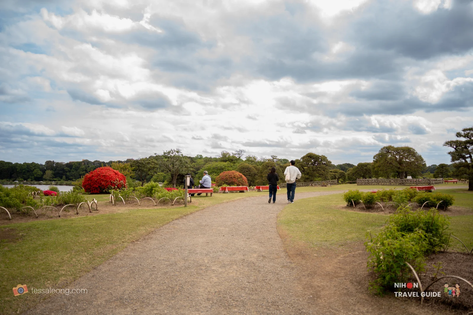 Scenic walking path through Kairakuen Garden with red azaleas, green lawns, and Lake Senba in the background.