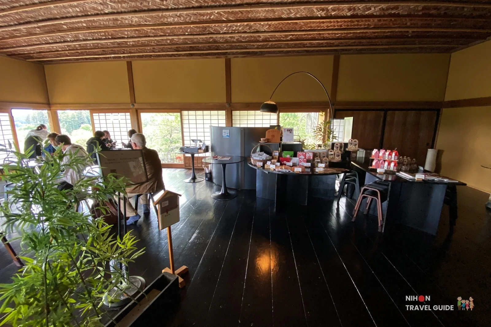 Spacious interior of Cafe Raku inside Kobuntei pavilion at Kairakuen Garden, showing high woven ceiling and visitors enjoying the historic space