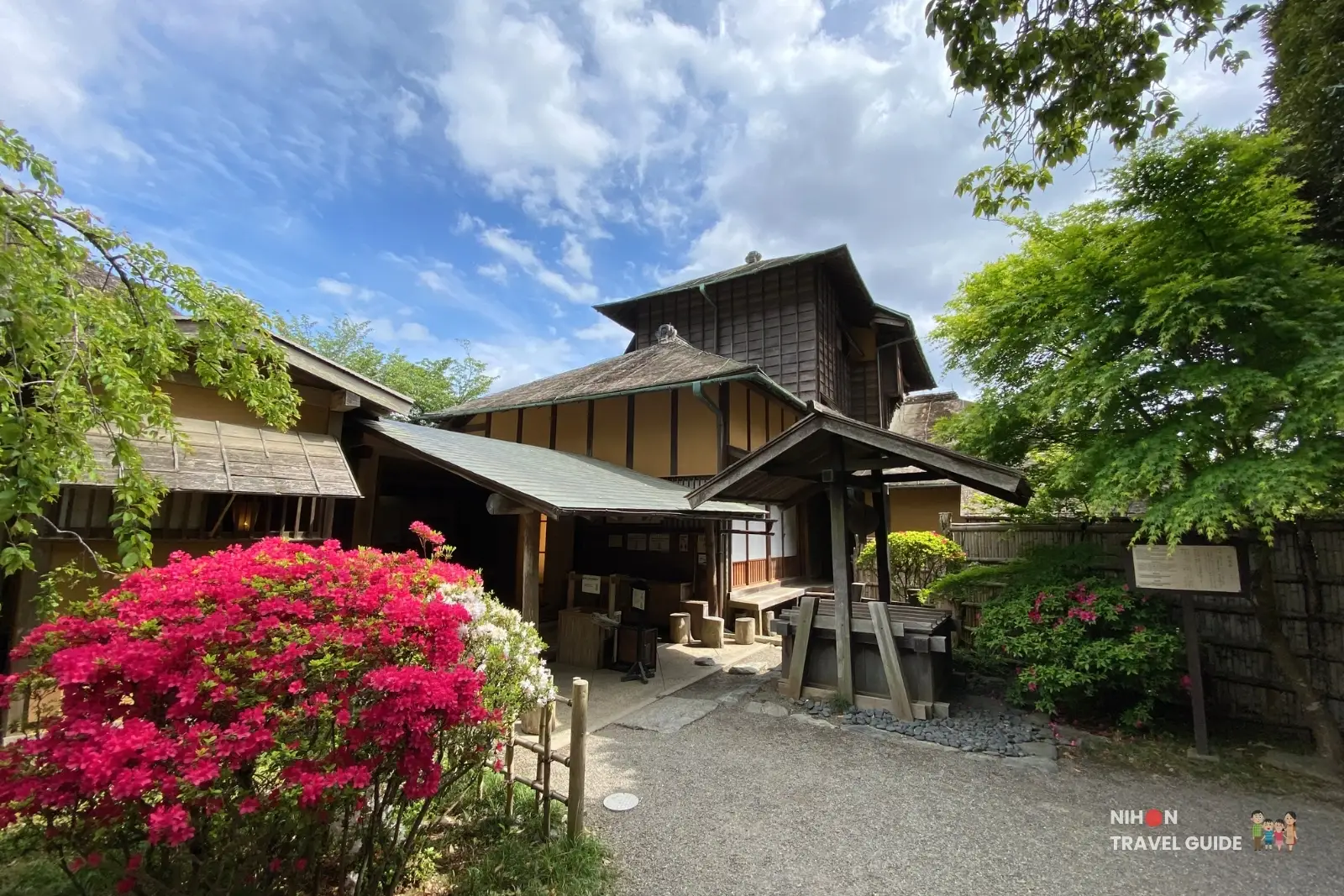 Exterior view of the historic three-story Kobuntei pavilion at Kairakuen Garden in Mito, surrounded by vibrant red azaleas and lush greenery.