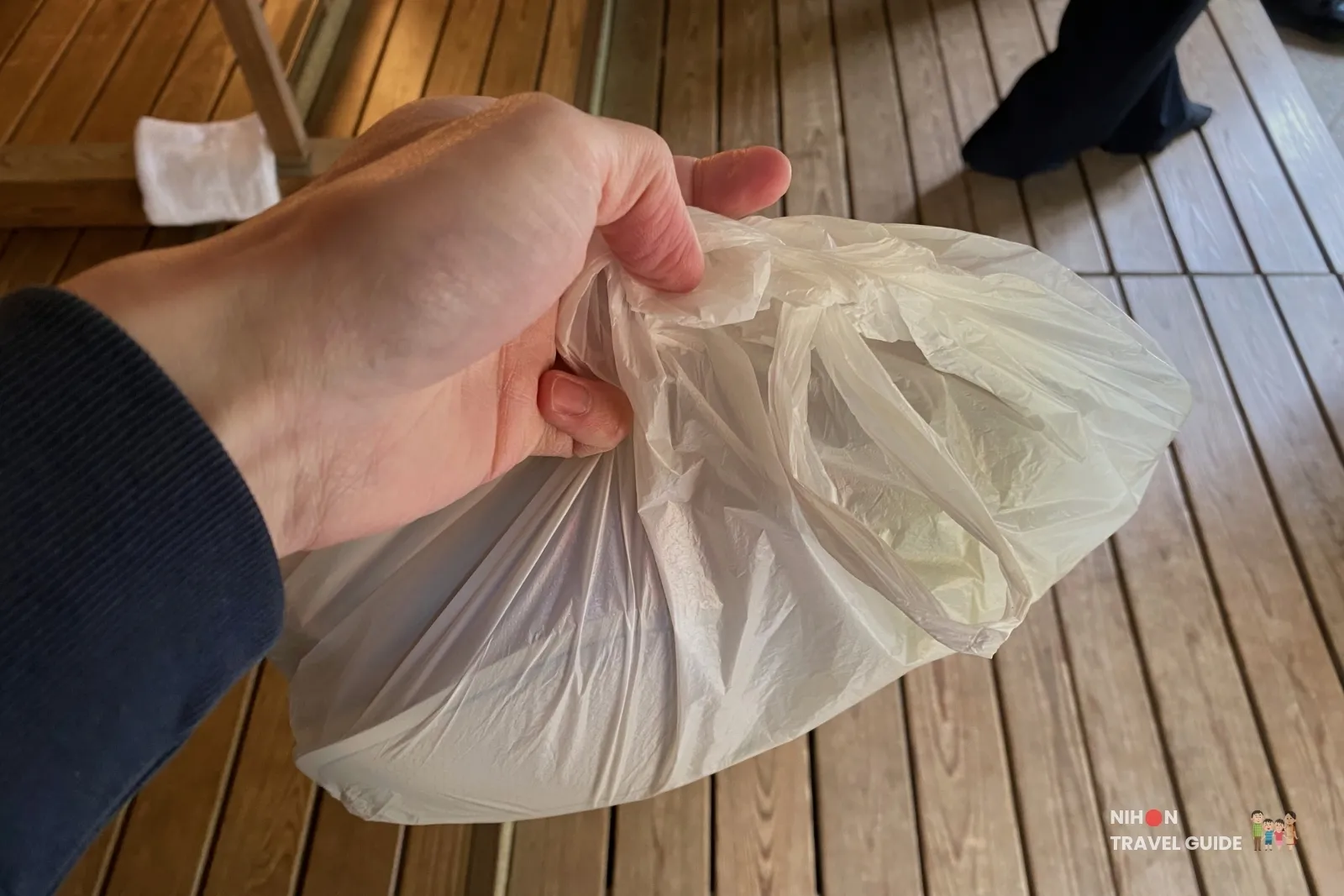 Visitor holding a plastic bag for shoes at Kobuntei pavilion in Kairakuen Garden, showing the common practice of removing shoes before entering.