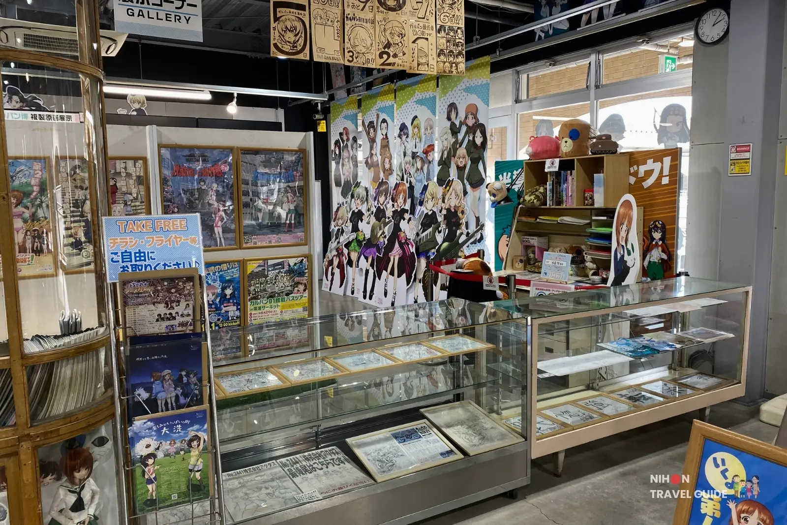 Display cases with artwork, posters, and collectibles inside Oarai Garupan Gallery.