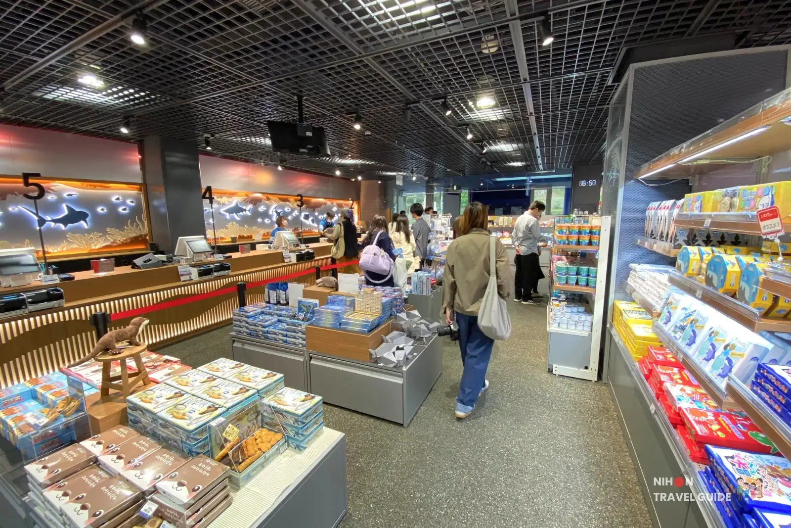 Interior of Souvenir Shop Moramora at Aqua World Ibaraki Oarai Aquarium showing checkout counters, snack displays, and visitors shopping