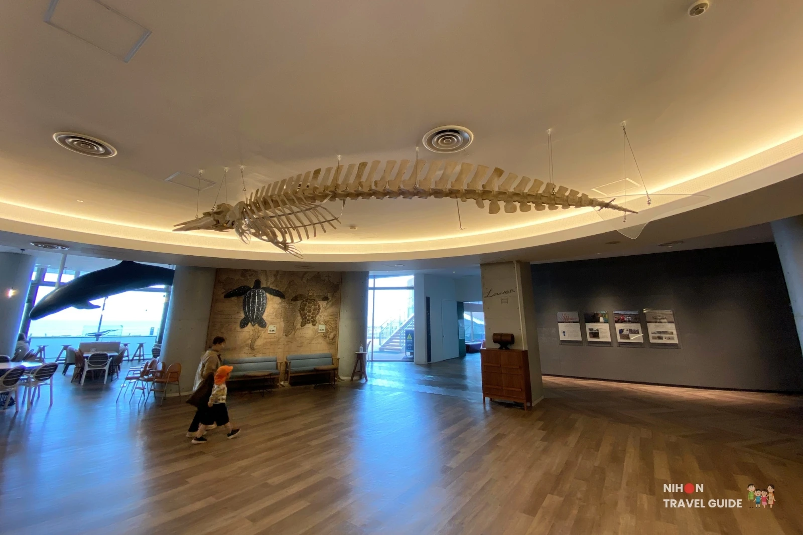 Large whale skeleton suspended from the ceiling in the lounge area at Aqua World Ibaraki Oarai Aquarium, with turtle wall art and seating