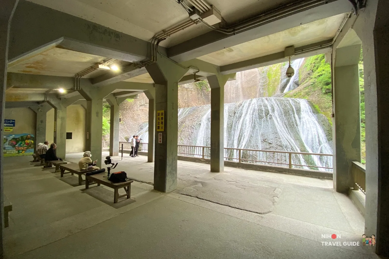 Interior of the first-level observation deck at Fukuroda Falls, with visitors resting on benches and a clear view of the cascading waterfall