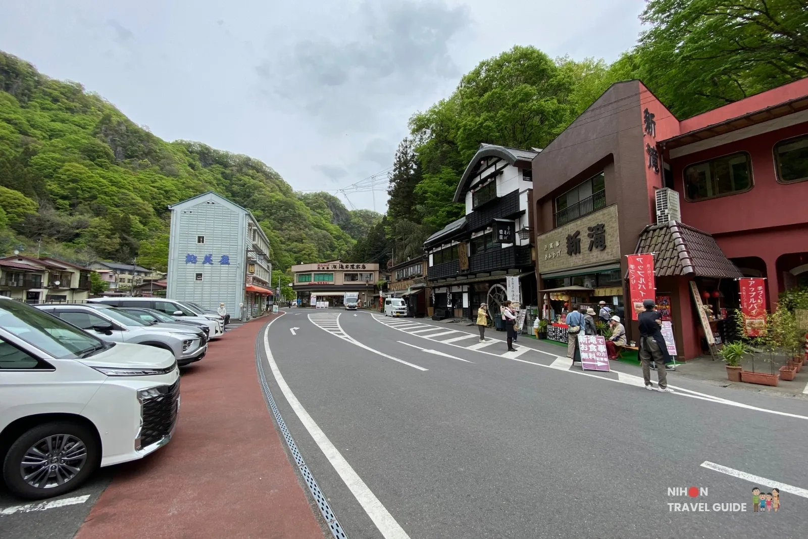 fukuroda-falls-parking-and-shops-area Parking area and shops near the entrance to Fukuroda Falls, with traditional buildings, parked cars, and forested hills in the background