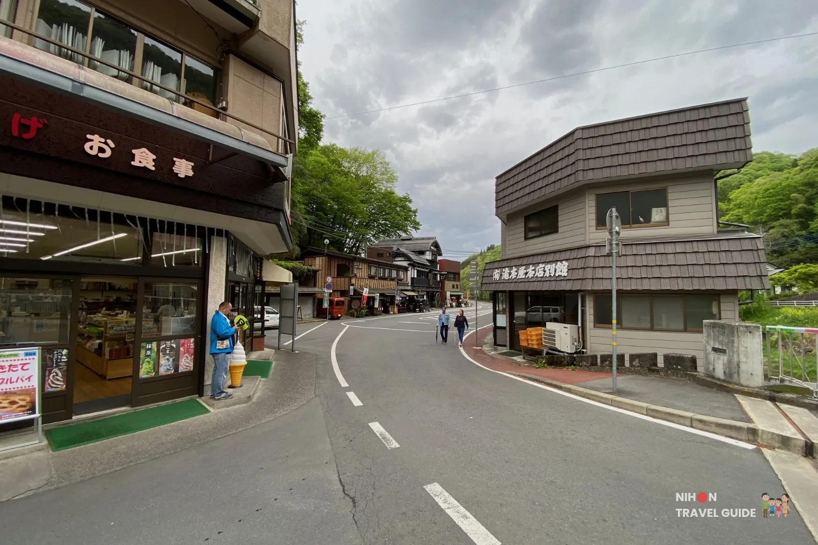 Street view of the shops and restaurants near Fukuroda Falls entrance, with visitors and forested hills in the background.