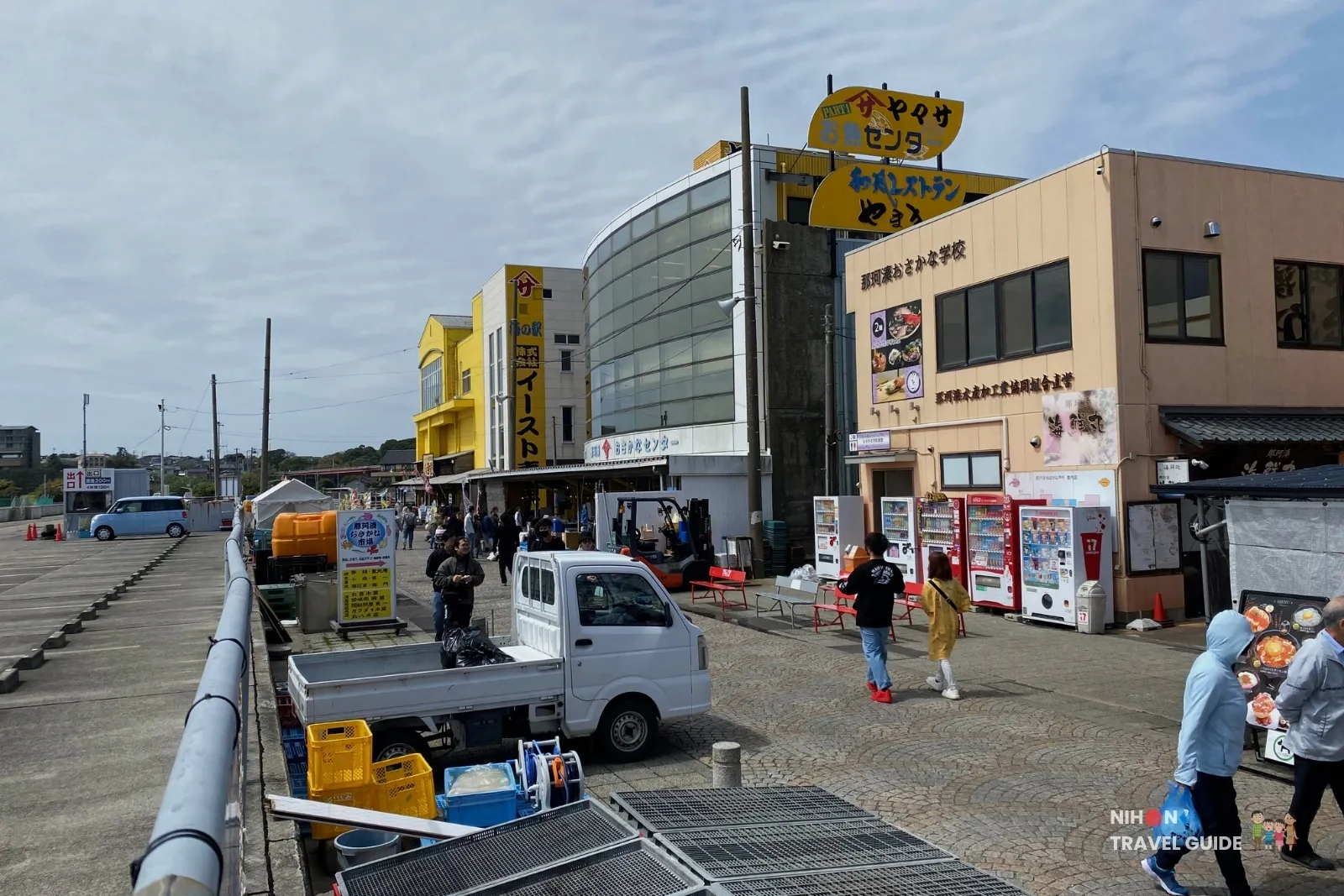 Overview of the main shopping and dining area at Nakaminato Fish Market in Hitachinaka, Ibaraki, showing colorful shop buildings, visitors, and market stalls along the waterfront