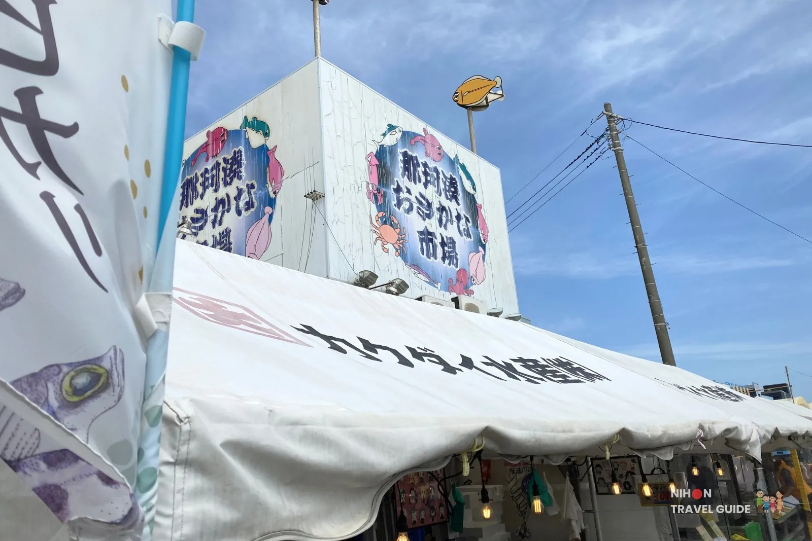 Colorful entrance to Nakaminato Fish Market (那珂湊おさかな市場) in Hitachinaka, Ibaraki, with large banners, white tents, and seafood shop signs under a blue sky