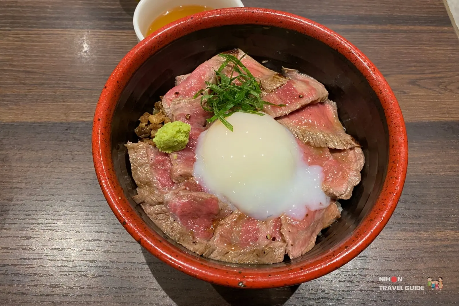 Aso Akaushi beef rice bowl (akagyu don) topped with rare sliced beef, soft-boiled egg, wasabi, and green onions at a restaurant in Sakura Machi Kumamoto.