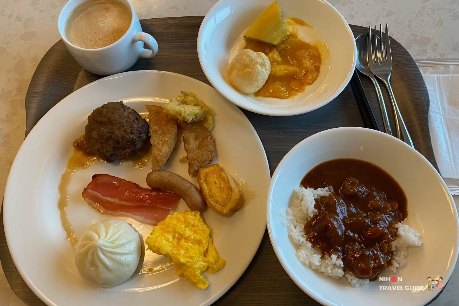 Breakfast buffet plate at KOKO HOTEL Premier Kumamoto featuring horse meat curry, Akaushi hamburger steak, scrambled eggs, bacon, sausage, steamed bun, and local side dishes.