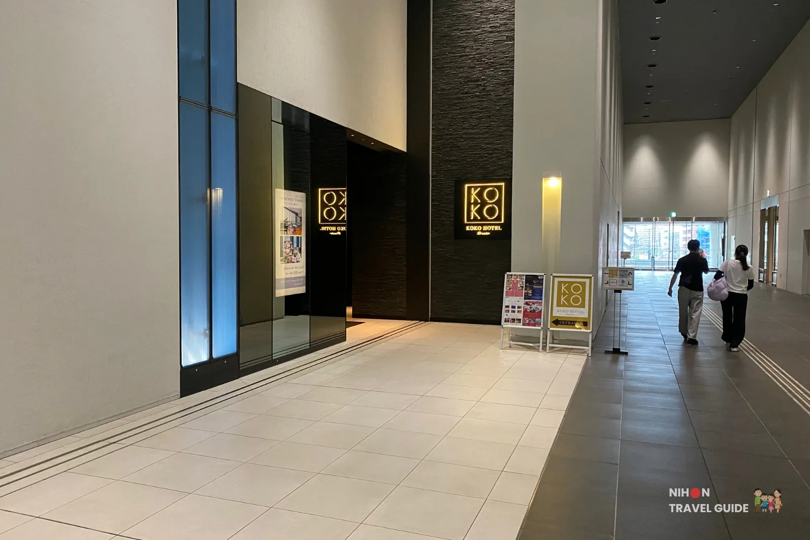 Main entrance and corridor of KOKO HOTEL Premier Kumamoto inside Sakura Machi, with illuminated KOKO HOTEL signage.