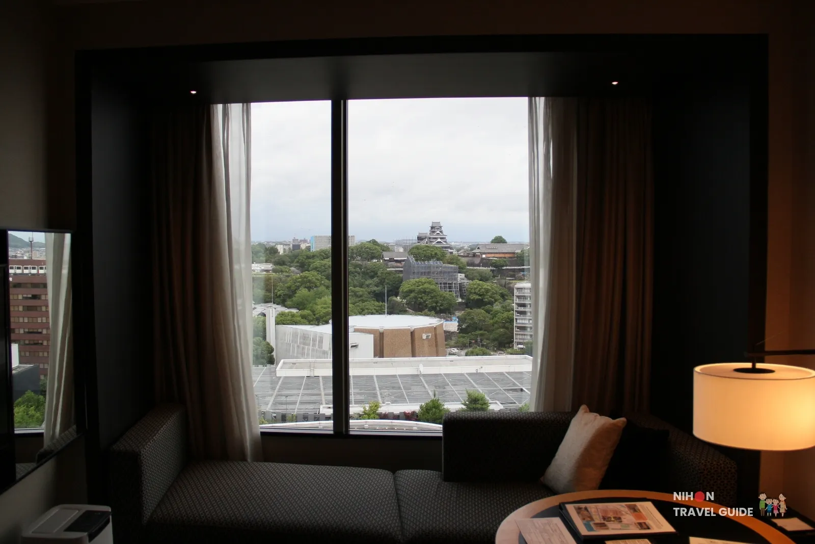 View of Kumamoto Castle from a guest room at KOKO HOTEL Premier Kumamoto, seen through large windows with a sofa seating area in the foreground.