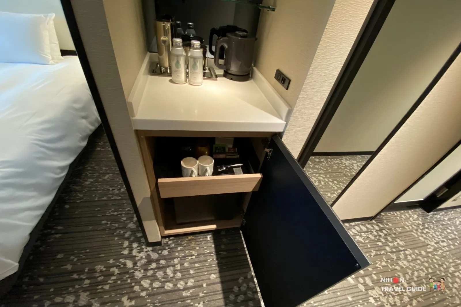 koko-hotel-premier-kumamoto-room-minibar-kettle In-room amenities at KOKO HOTEL Premier Kumamoto, including electric kettle, complimentary bottled water, mugs, tea and coffee supplies, and mini-fridge.