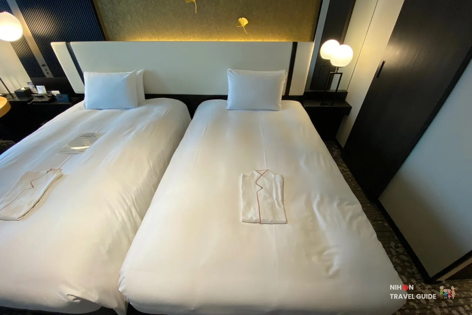 Twin beds in the Superior Twin room at KOKO HOTEL Premier Kumamoto, with neatly folded yukata, modern headboard, and gold ginkgo leaf accents.