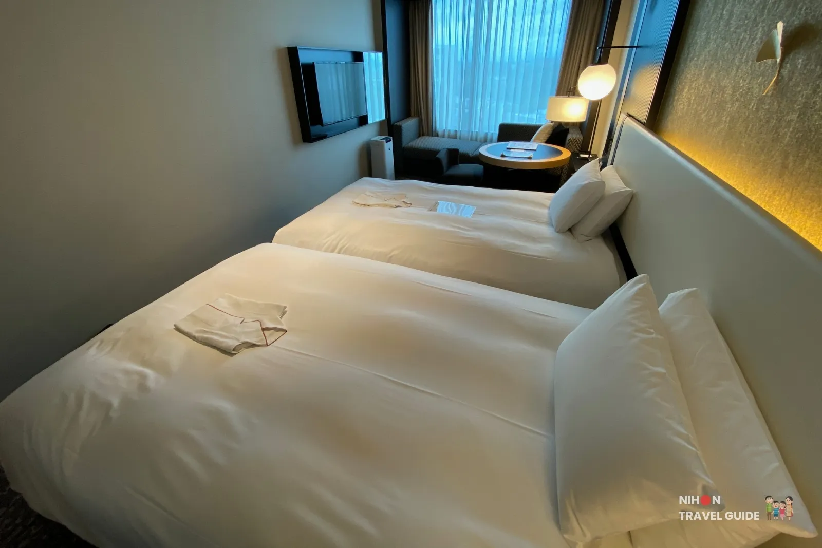 Overview of the Superior Twin room at KOKO HOTEL Premier Kumamoto, showing two beds, wall-mounted TV, and seating area by the window.