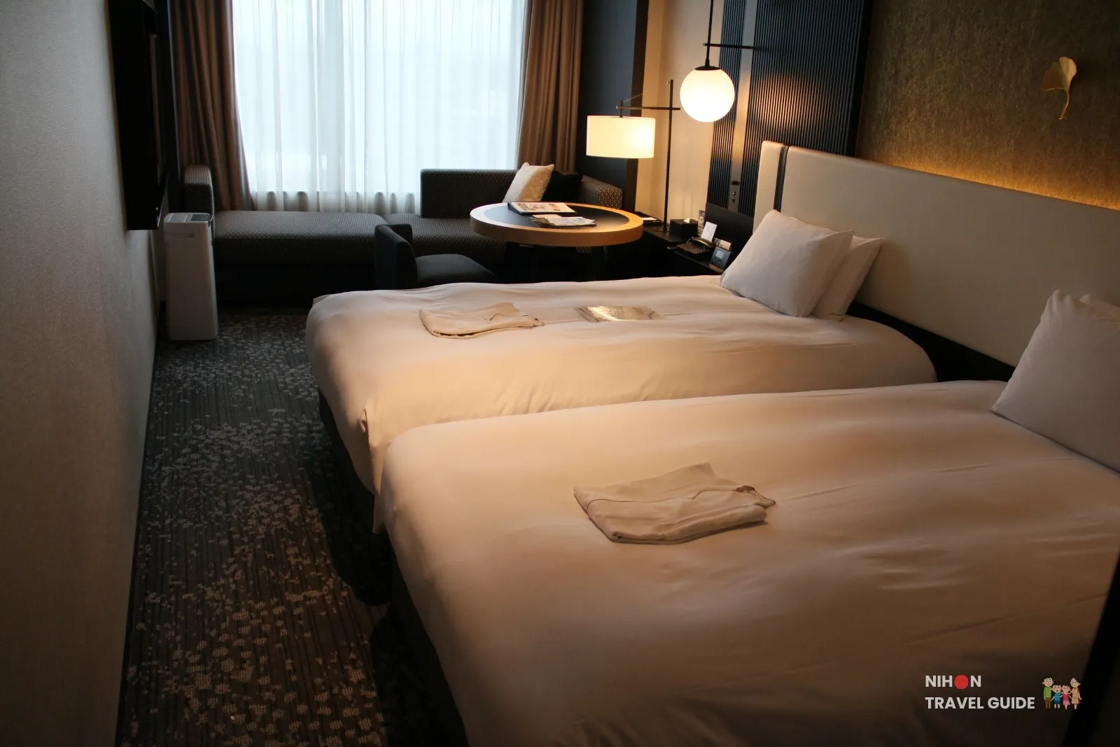 Side view of the Superior Twin room at KOKO HOTEL Premier Kumamoto, showing two beds, sofa seating area by the window, and modern lighting.