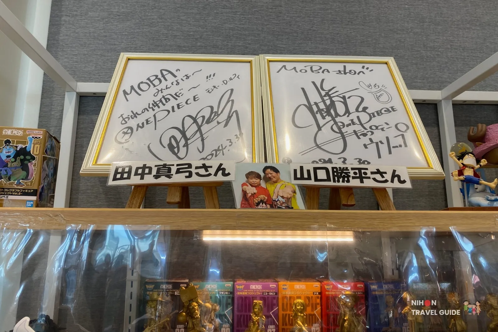 Framed autographs from Mayumi Tanaka (Luffy) and Kappei Yamaguchi (Usopp) on display at OKAGESAMA MOBA near the Jinbe statue in Kumamoto