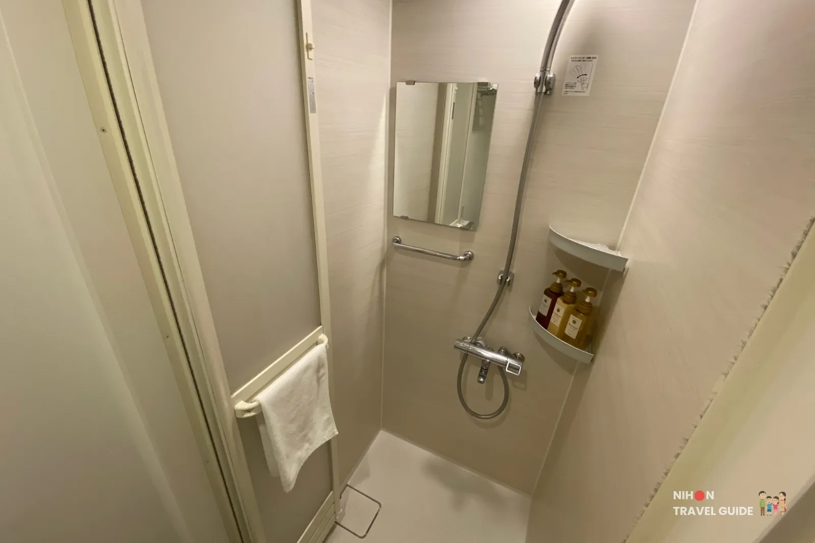Compact shower booth in the Single Room with Shower Booth at REF Kumamoto by Vessel Hotels, showing handheld shower, toiletries shelf and small mirror