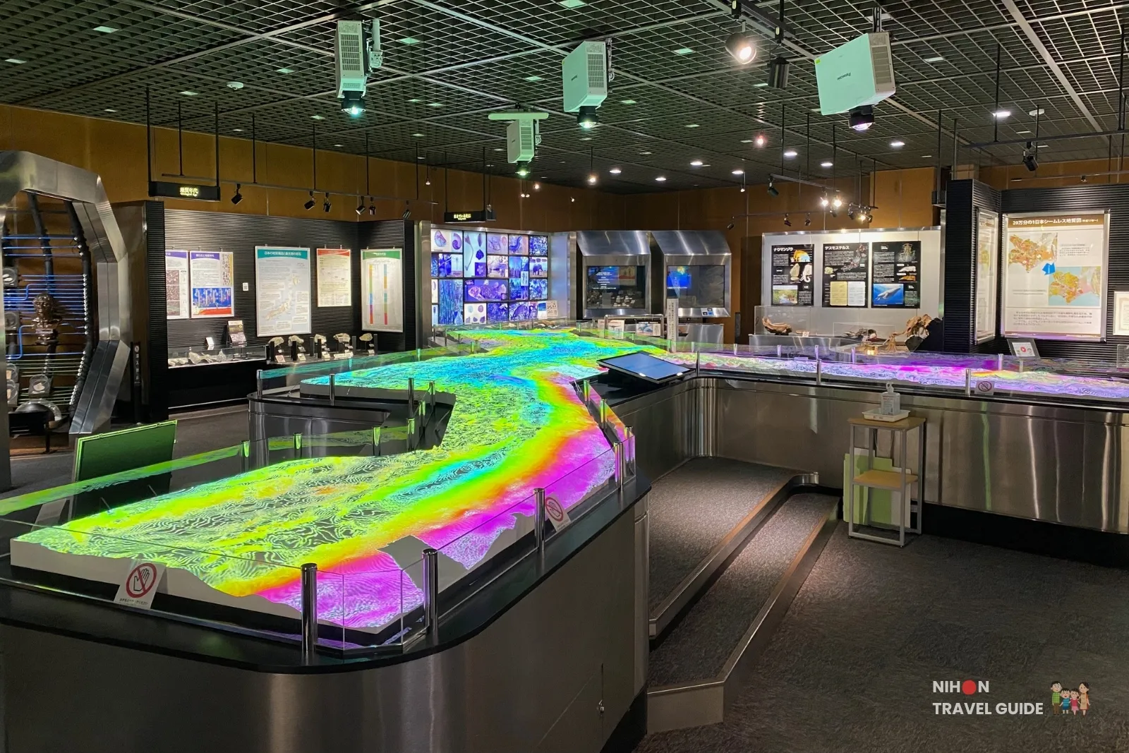 Wide interior view of Exhibition Room 1 featuring the large illuminated 3D geological model of the Japanese Islands with colorful projection mapping at the Tsukuba Geological Museum.