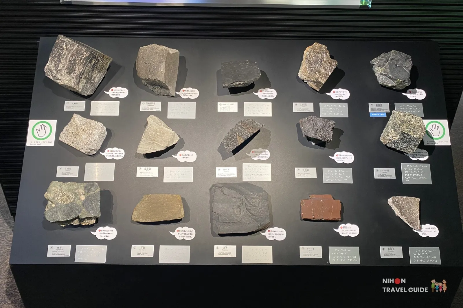 Interactive display of various rock specimens that visitors can touch in Exhibition Room 1 of the Tsukuba Geological Museum, with Japanese labels explaining each rock type.